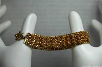 Front view of gold tone mesh chain bracelet displayed on white stand showing overall length and width.