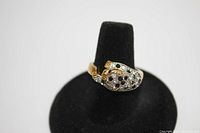 Front view of gold tone leopard ring displayed on black stand showing clear and black stones simulating spots.