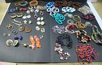 Overview of jewelry lot spread on black background showing necklaces, earrings, and bracelets in various colors and materials