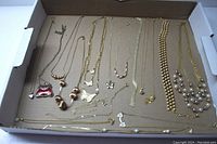 Photo showing arrangement of 17 gold chain necklaces of various styles and lengths laid out in a flat box.