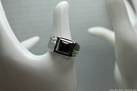Front angled view of silver tone men's ring with black stone, showing square stone and mixed matte grey and silver sides.