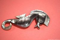 Image of sea horse brooch in gray and pearl tones on red background, showing curled tail and detailed fins, highlighting mother of pearl material and colors.