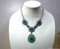 Full view of the costume necklace on display bust, showing the chain and pendant design with green enameling and blue cabochons.