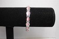 Front view of silver tone bracelet showing pink cabochons, presented on black display stand.