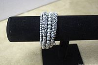 View of the silver tone multi-size beaded spring wire bracelet displayed on black stand, showing the coiled design and various sized round beads and disc beads.