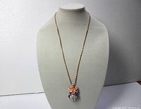 Full view of necklace on display bust showing gold-tone box link chain and colorful owl pendant.