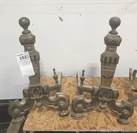 Pair of heavy decorative fireplace andirons with a classical design, seen from front on a wooden surface.