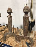 Pair of cast iron fireplace andirons showing overall wear and rust.