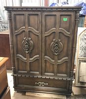 Front view showing ornate double doors with carved wood details and a bottom drawer with decorative handle.