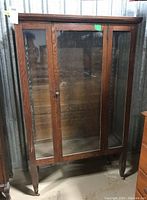Full front view of vintage wooden cabinet showing glass panels and door with knob, on casters.