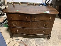 Front view of wooden dresser showing four drawers with mixed hardware pulls in a woodgrain finish.