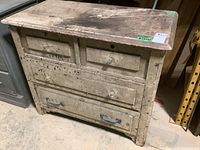 Front view of the entire wood dresser showing four drawers with mixed hardware and heavily worn surface.