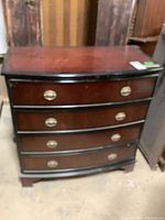 Front view of wooden dresser showing four drawers with brass handles and curved front surface.