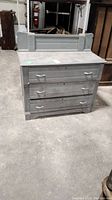 Full front view of the gray painted three-drawer dresser showing overall shape, style, and dusty surface.