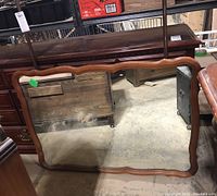 Photo showing front view of large rectangular dresser mirror with wooden scalloped frame and reflection of surrounding room.