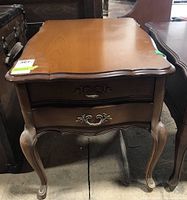 Front view of rectangular wood end table with scalloped edge top, two front drawers with metal pulls, and curved legs.
