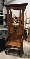 Front view showing the full wood hall tree bench with mirror and hooks, carved floral patterns on the upper frame, and decorative carved lower panel with central spoke broken.