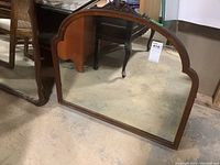 Front view of wood framed mirror positioned on floor showing decorative top carving and side spindle holes.