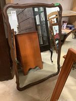 Front view of wooden framed mirror with wavy edge, showing the mirror glass and some surrounding furniture reflected.
