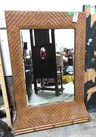 Full view of large wicker framed mirror with beveled glass showing its height and base detail.