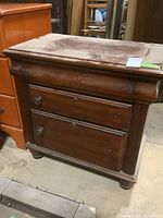 Photo showing wood nightstand with two drawers, keyholes, round metal knobs, surface scratches and dust.