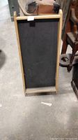 Front view of a rectangular wooden framed black noteboard standing vertically on floor.