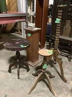 Four wooden furniture pieces including a square column pedestal and three tripod-based round pedestal stands of varying heights.