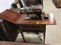 Singer sewing machine mounted on wooden table with drawer, showing overall wear and condition