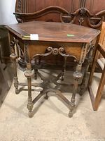Front and side view of the wood table showing six spoked spindle legs, decorative apron trim, and surface wear.