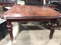 Front view of square wooden table showing wear and casters on legs.