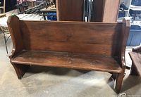 Front view of wood church pew showing full length seat and backrest with wear and scratches.