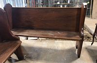 Full view of wooden church pew showing side profile and back hymnal rack