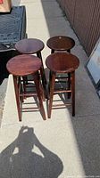 Four wooden bar stools arranged outdoors, front angle view.