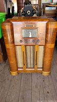Front view of the Marconi antique floor radio showing the wooden cabinet, control knobs, tuning dial, and fabric speaker grill.