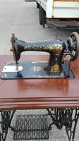 Vintage Singer sewing machine with gold detailing on black body, mounted on wooden table with treadle base.