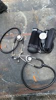 Photo showing two black stethoscopes and one blood pressure cuff with gauge and bulb on table surface