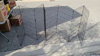 Full length shot of black metal folding dog pen with six panels laying on side on pavement outdoors.