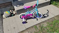 Side view of little girl's bike showing blue frame, pink seat and chain guard, white tires, and training wheels
