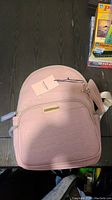 Front view of pink Juicy Couture backpack with embossed text and gold metal plaque on front pocket