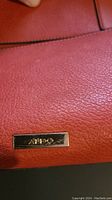Close-up of Aldo brand plaque on textured orange leather surface of purse