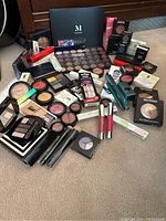 Full assortment of makeup products spread out, showing palettes, brushes, nail lacquer, lip products and compacts.