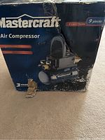 Mastercraft air compressor box showing product name, specifications including 2-gallon tank capacity and 1/3 peak HP motor, labeling the set as 9 pieces.