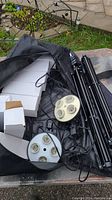 Photo showing black tripods, circular light fixtures with four sockets, power cords, and some boxed items including bulbs.