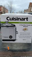 Box front showing Cuisinart 4-Cup Rice Cooker & Steamer with features listed including nonstick aluminum pot, stainless steel steamer basket, cook/warm switch with indicator lights, and BPA free. Model CRC-400.