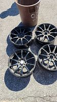 Four black 18 inch car rims on pavement, showing their 10-spoke design, lightly used condition.
