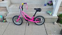 Side view of the pink Supercycle Kickstart little girls bike placed against concrete steps.