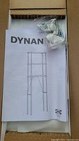 Open box showing assembly instructions and hardware bag for IKEA DYNAN stand