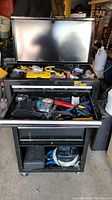 Photo of the opened black metal rolling tool box with various hand tools in the compartments and drawers.