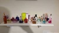 Wide shot displaying 14 bottles of women's perfumes and skin care sprays arranged on a white shelf.