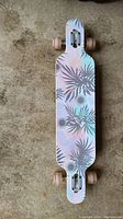 Top view of the longboard showing pastel floral design on deck with grey leaf patterns on a light background.